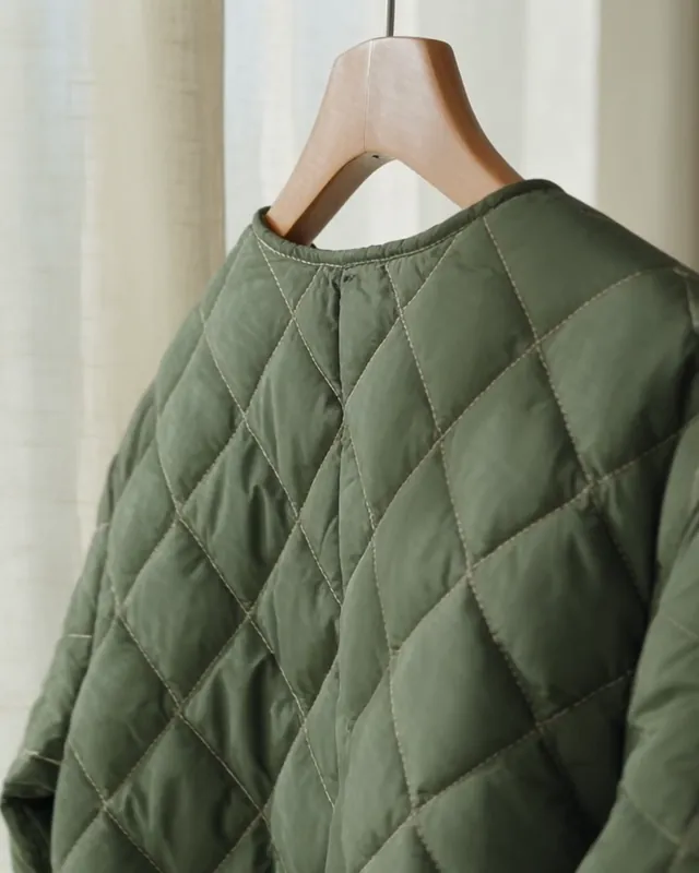 Close-up of a forest-green quilted jacket on a wooden hanger in soft morning light.